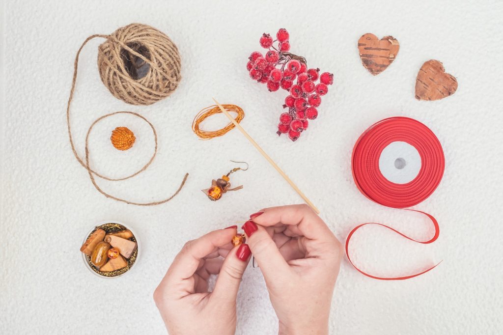 Handmade Jewelry, DIY flat lay in red and brown. Jewelry designer workplace. Woman hands making